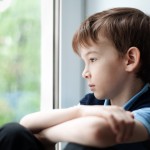 Sad boy sitting on window